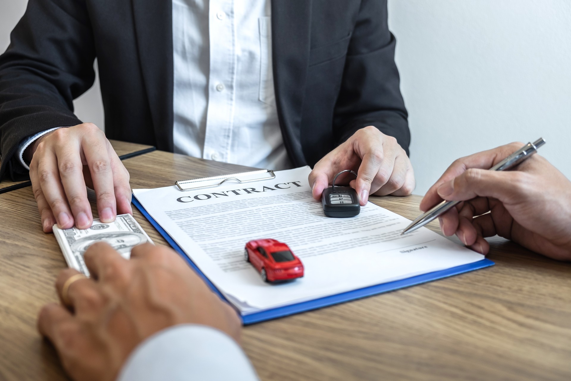 Car rental and Insurance concept, Young salesman receiving money and giving car's key to customer after sign agreement contract with approved good deal for rent or purchase